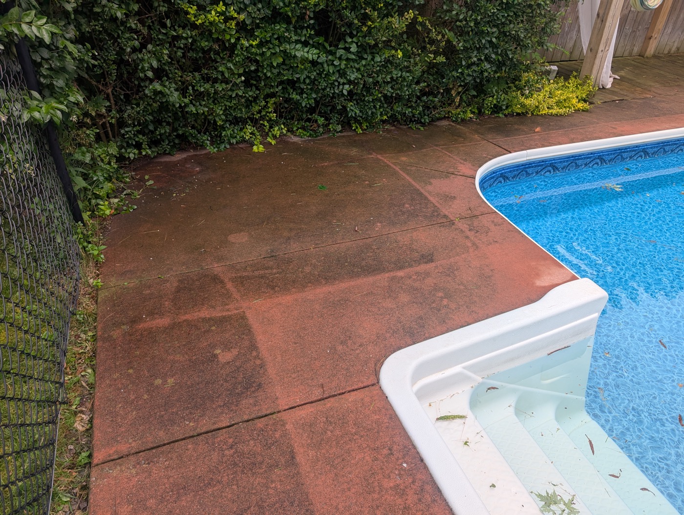 Pool deck concrete before pressure washing, dark with dirt and staining